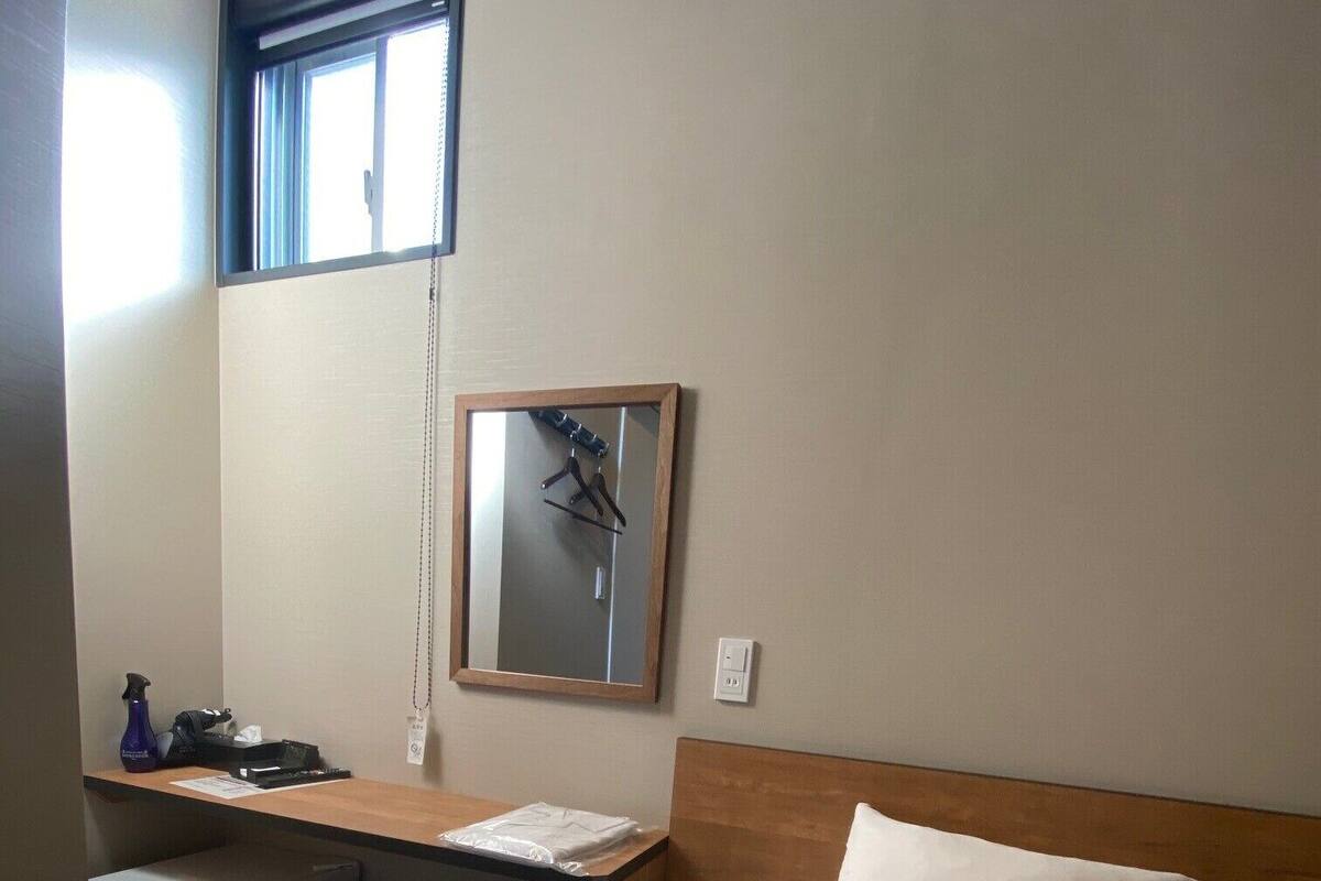 A hotel room with a bed, a desk, a chair, a small refrigerator, a mirror, and a window.