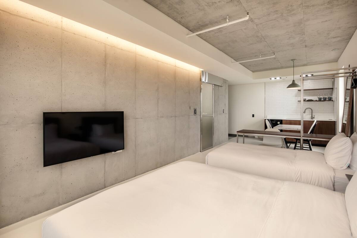 Une chambre d’hôtel moderne équipée d’un téléviseur à écran plat fixé au mur, d’une petite kitchenette et d’un lit avec un oreiller.