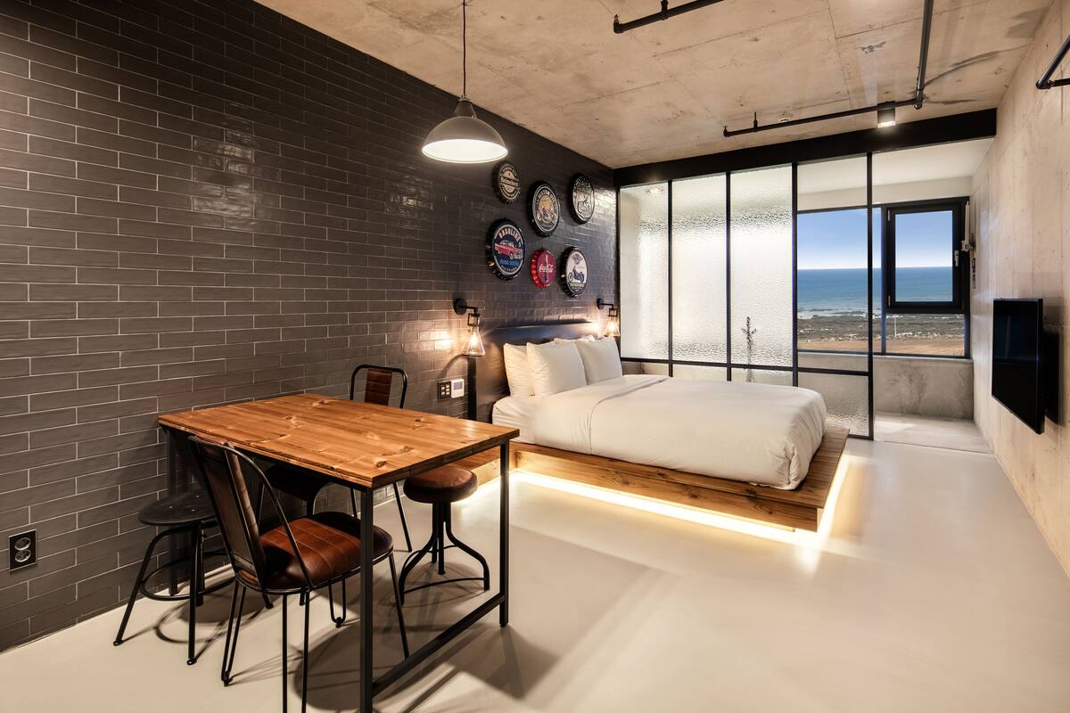 Une chambre moderne avec un mur en briques, une table à manger en bois et un lit donnant sur l’océan.