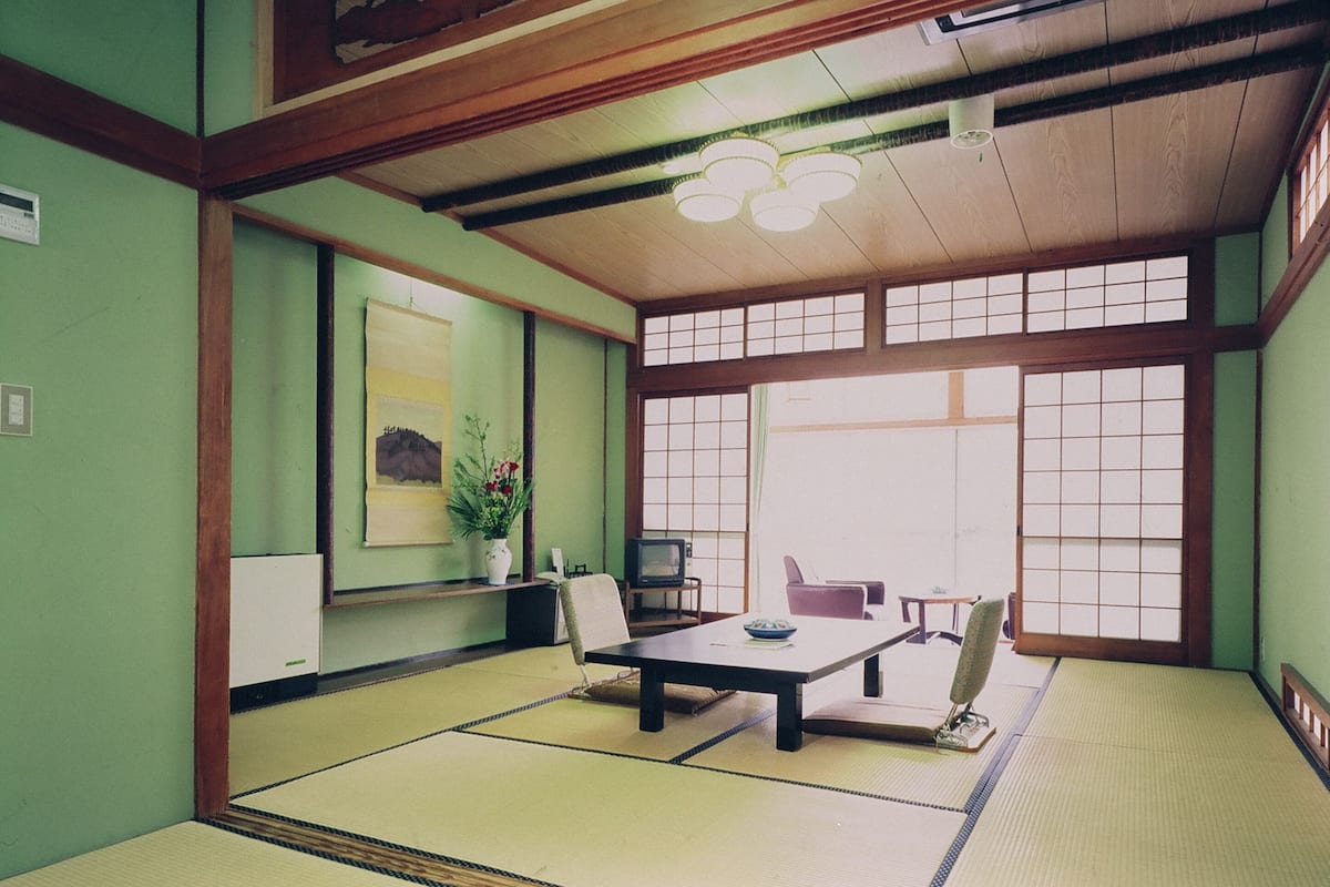 A traditional Japanese room with tatami flooring, a low table, a television, and a large window.