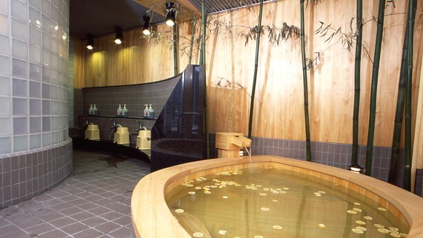 Un área de spa con una bañera de madera llena de monedas, una pared de bambú y un suelo de baldosas.
