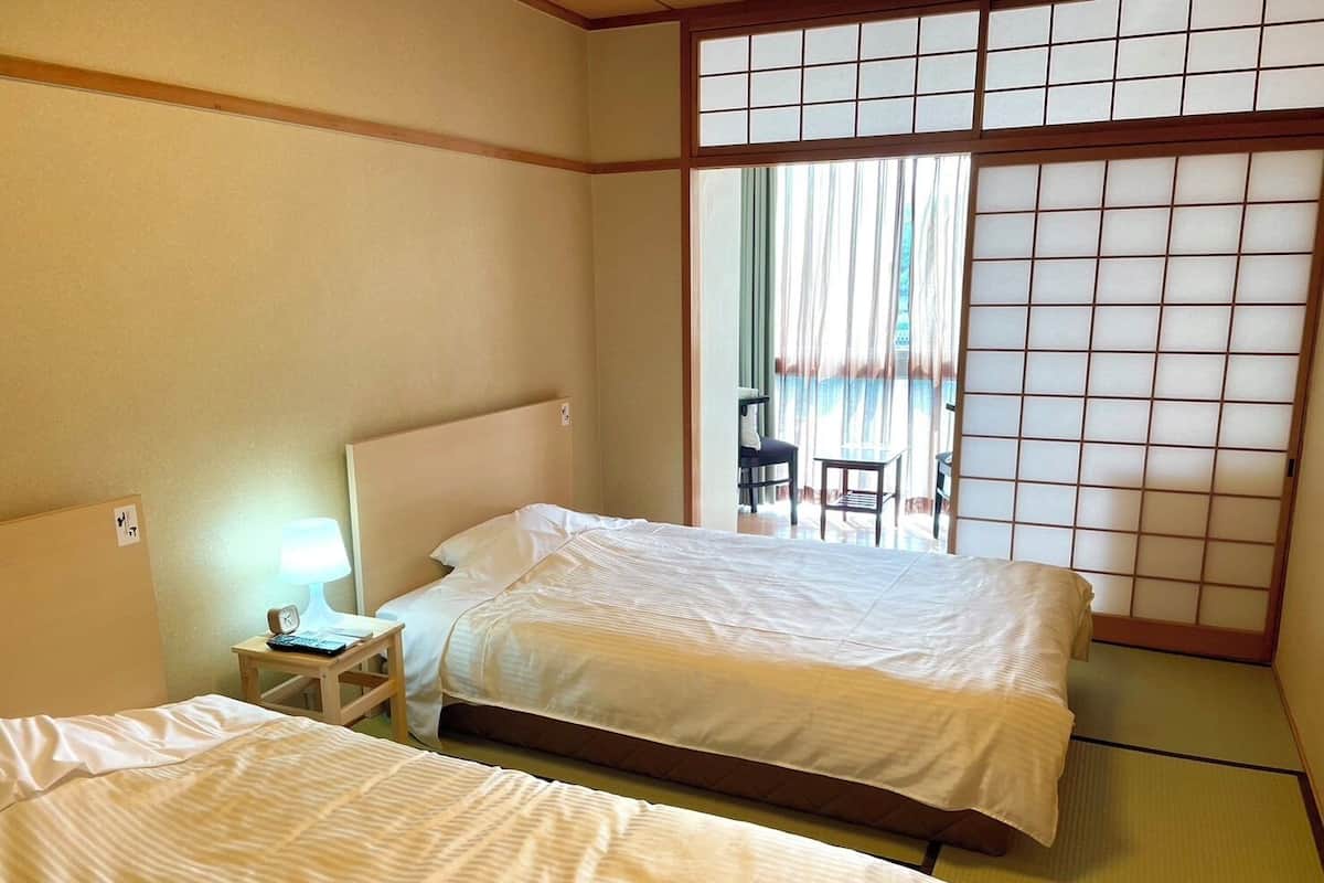 A hotel room with two beds, a small bedside table with a lamp, and a sliding shoji screen door.