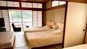 Habitación de hotel tradicional japonesa con suelo de tatami, dos camas, televisión y puerta corrediza que da a un balcón con vistas a una masa de agua.