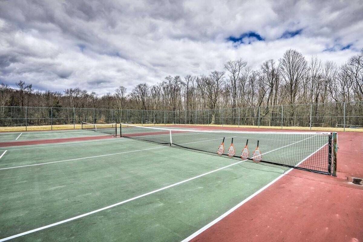 An outdoor tennis court with a net, surrounded by a fence and trees.