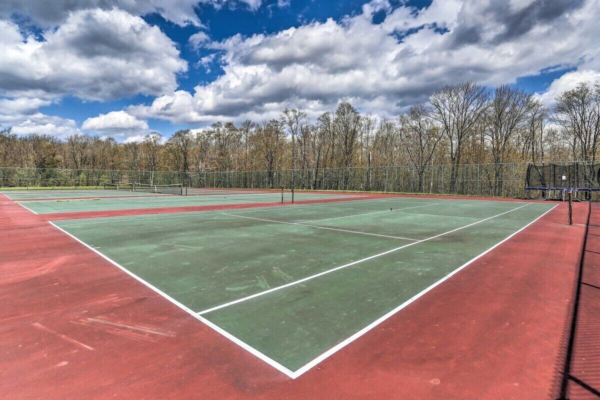 En tennisplan med nät, omgiven av träd och en klar himmel.