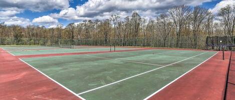 En tennisplan med nät, omgiven av träd och en klar himmel.