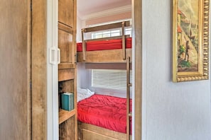 Una litera con colchón rojo, una escalera de madera y una ventana con persianas.