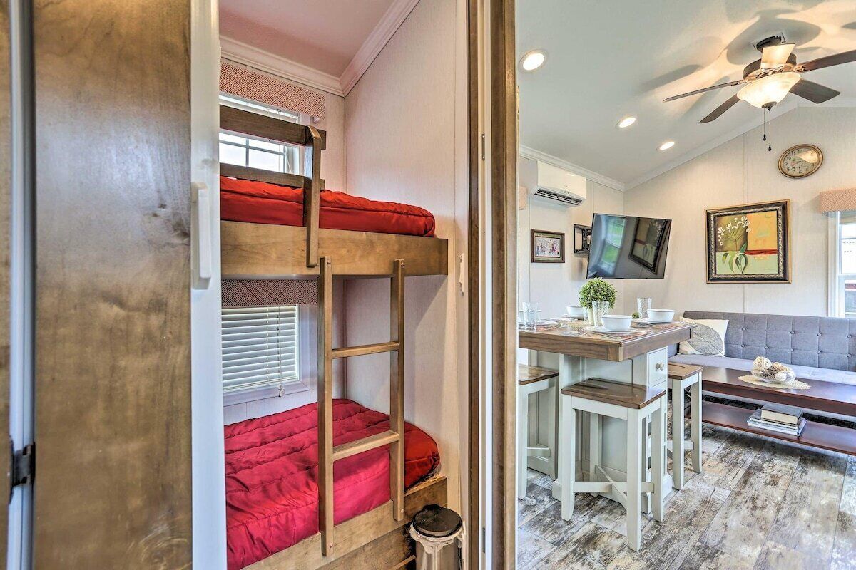 Un lit superposé avec un matelas rouge, un ventilateur de plafond et un coin repas avec une table et des chaises.