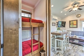 Una cama litera con colchón rojo, ventilador de techo y zona de comedor con mesa y sillas.