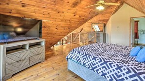 Una camera da letto con soffitto spiovente, un letto con lenzuola a fantasia, una televisione su un mobile in legno e una scala che conduce a un livello superiore.