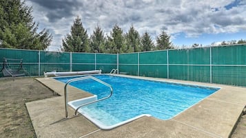 Une piscine rectangulaire avec un escalier en métal et une clôture verte qui l’entoure.
