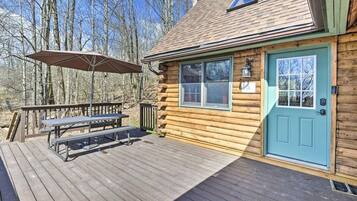 Une cabane en rondins avec une terrasse, une table de pique-nique et une porte.