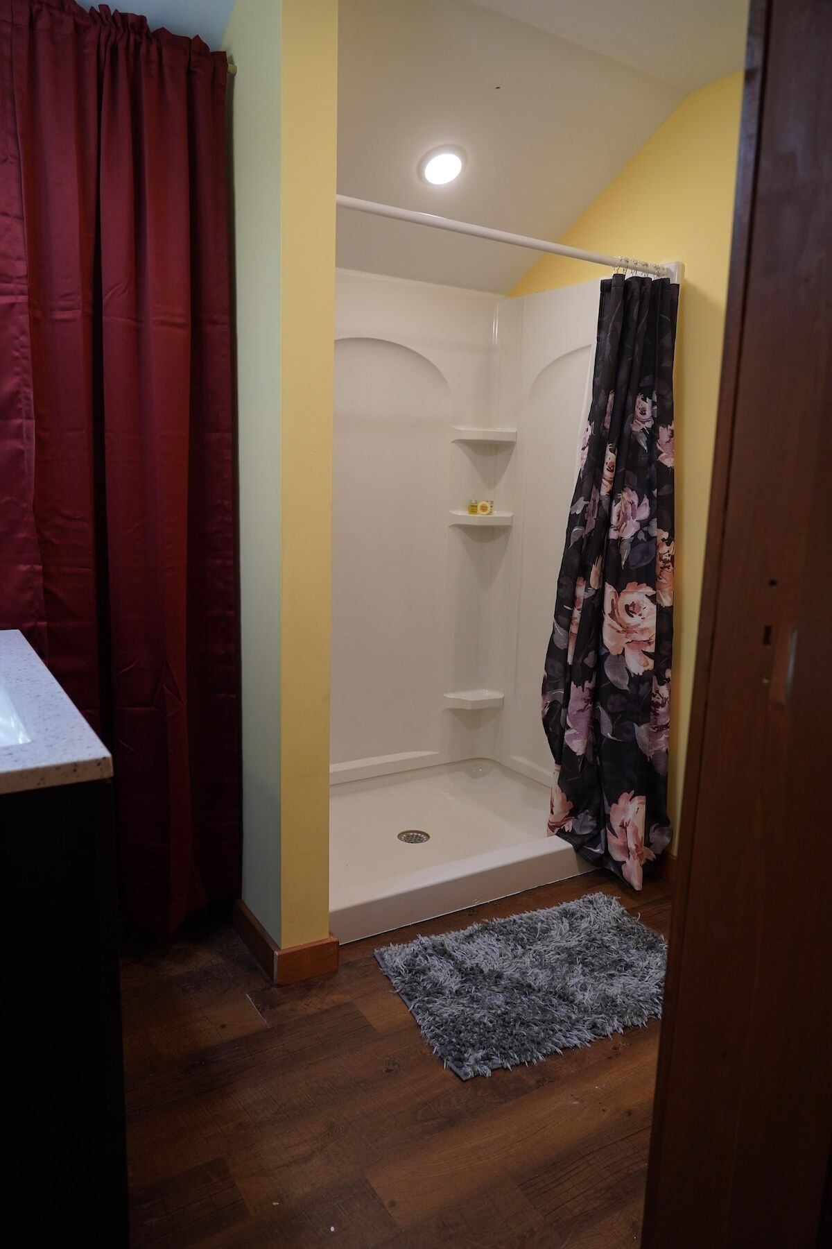Een badkamer met een douche, een houten vloer, een vloerkleed en een rood gordijn.
