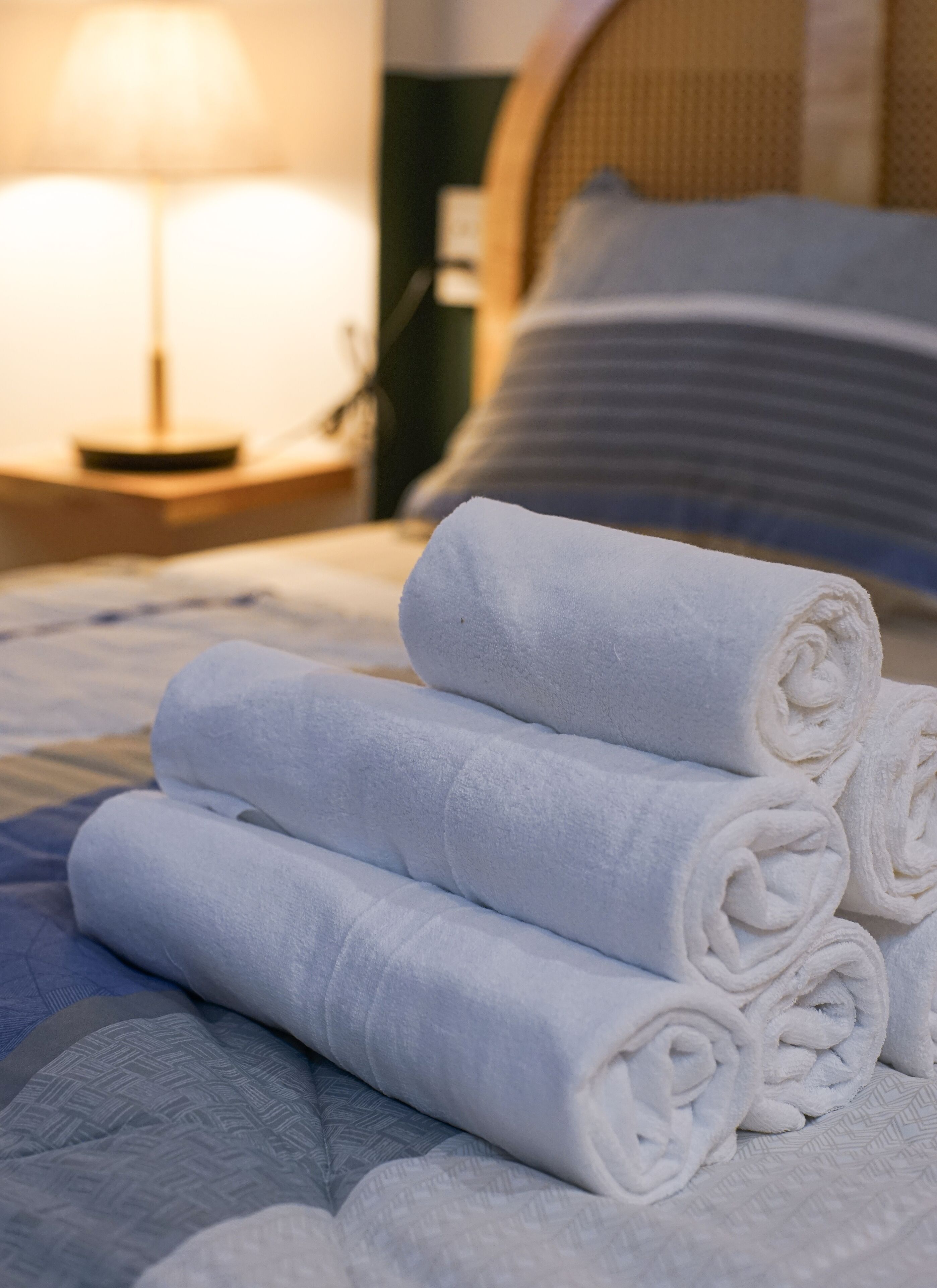 A neatly made bed with rolled white towels, a bedside lamp, and a striped pillow.