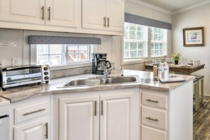 A kitchen with white cabinets, a built-in oven, a coffee maker, and a window with blinds.