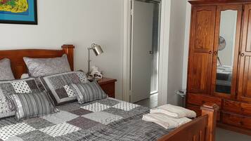 Une chambre à coucher avec un lit en bois, une table de chevet, une lampe, une armoire et une porte donnant sur une autre pièce.