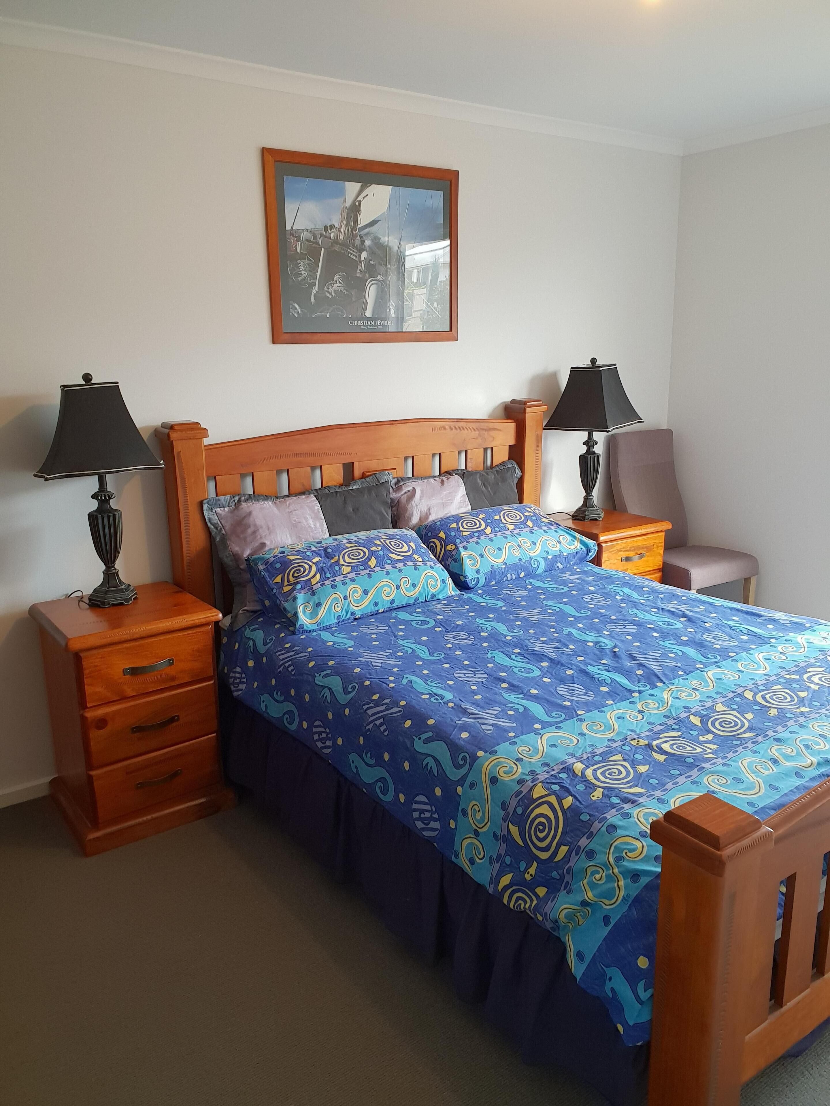 A bedroom with a wooden bed, two bedside tables with lamps, a dresser, and a framed picture on the wall.