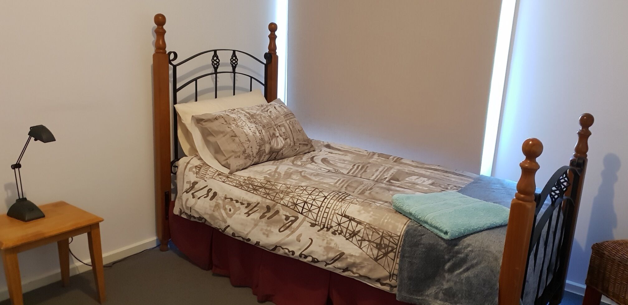 A single bed with a patterned bedspread, a bedside lamp, and a window with curtains.