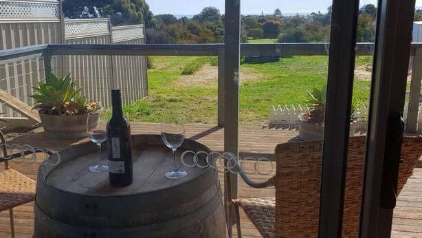 A wooden barrel with a bottle and two wine glasses on a balcony with a view of a grassy field and trees. -  Quite harbour village. Close to beach, boat ramp and attractions  (Penneshaw)