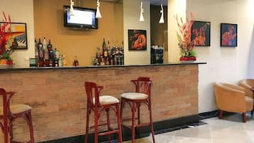 A bar area with a wooden counter, three bar stools, and a television mounted above.