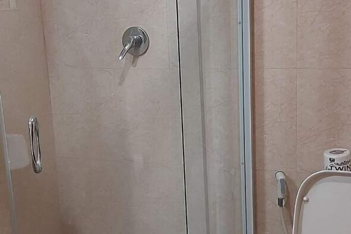 A bathroom with a glass-enclosed shower, a toilet, and a towel on the floor.