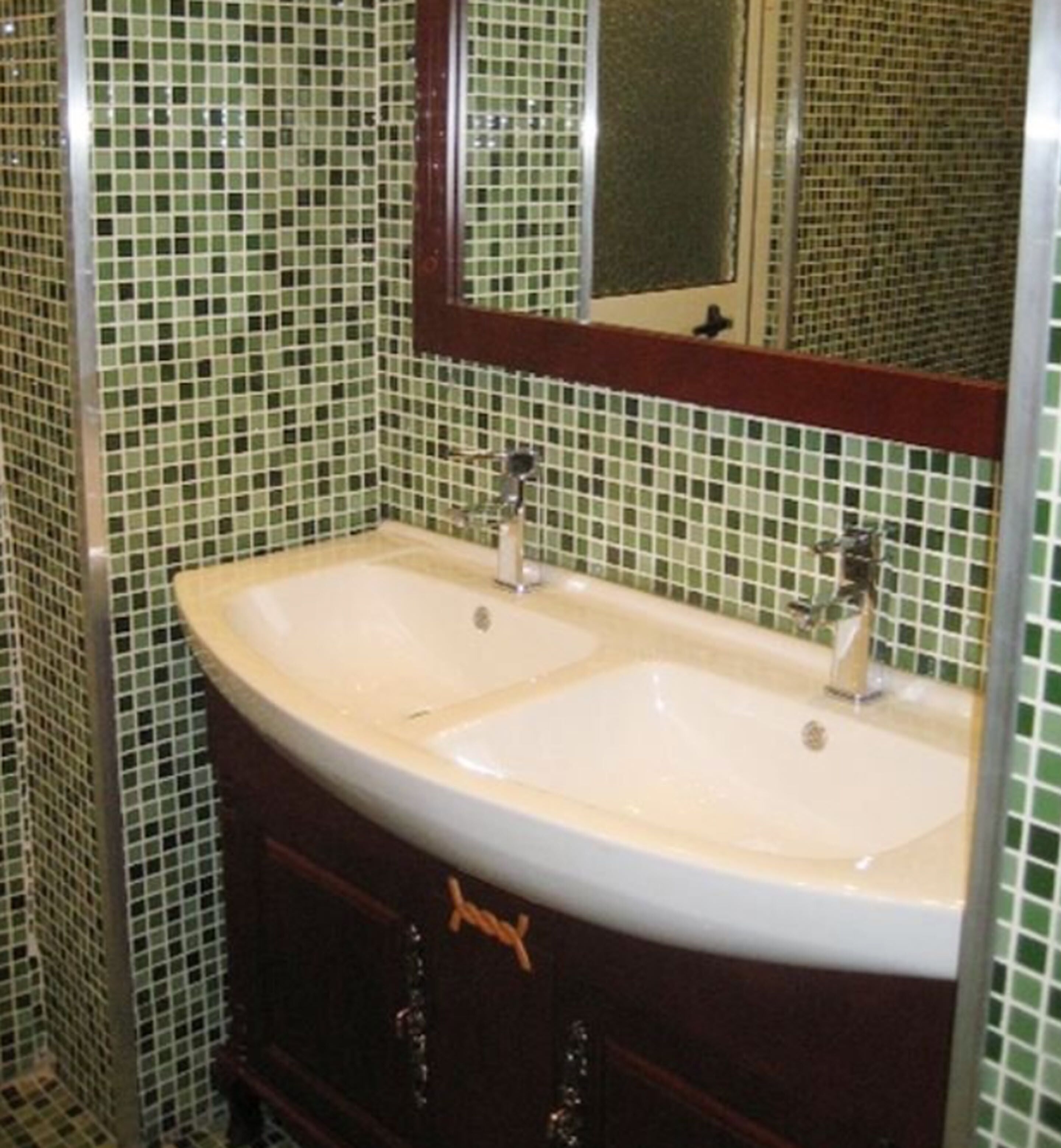 A bathroom with a double sink, a mirror above it, and green mosaic tile walls.
