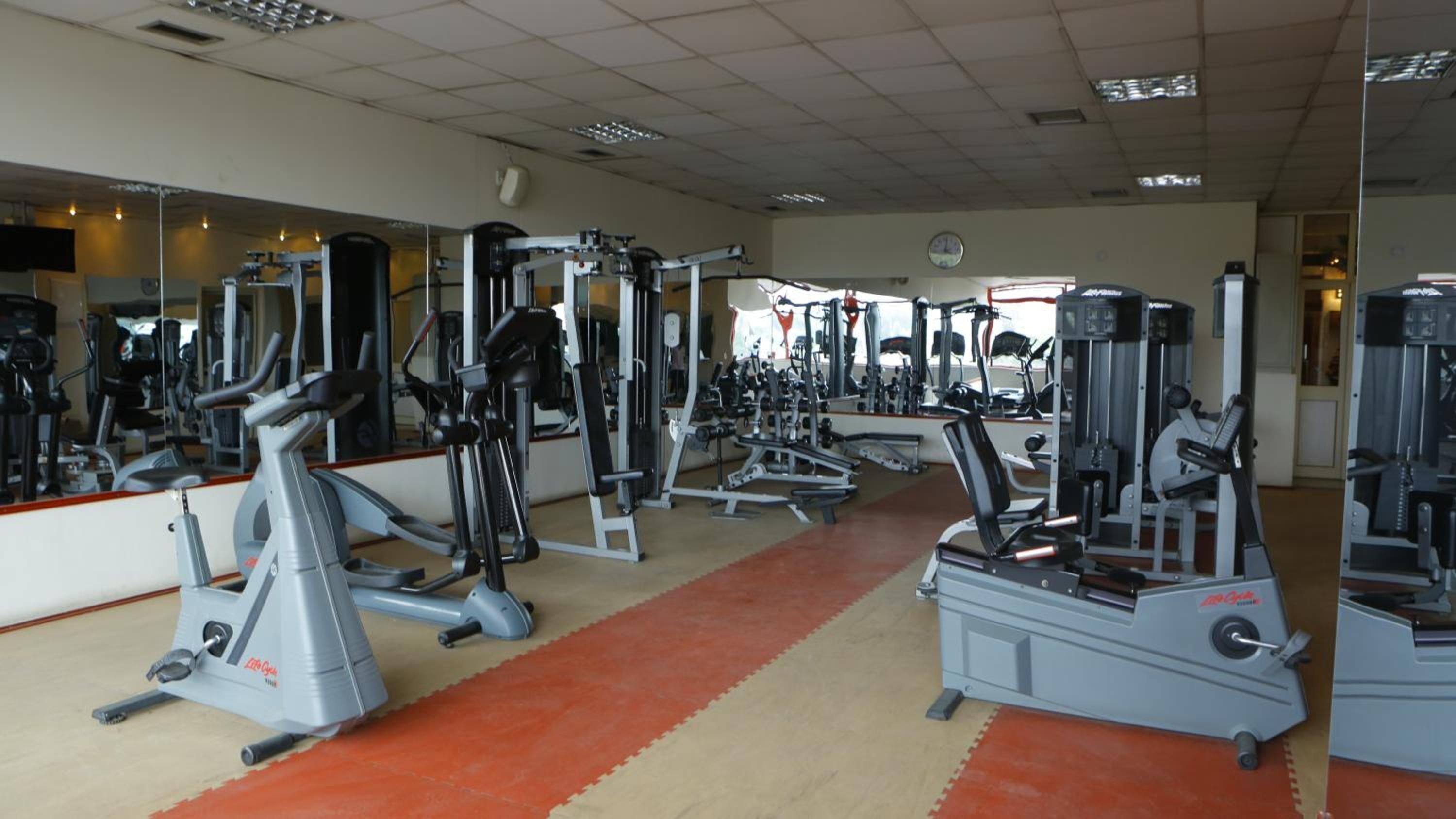 A gym with various exercise machines, mirrors, and a red carpeted floor.