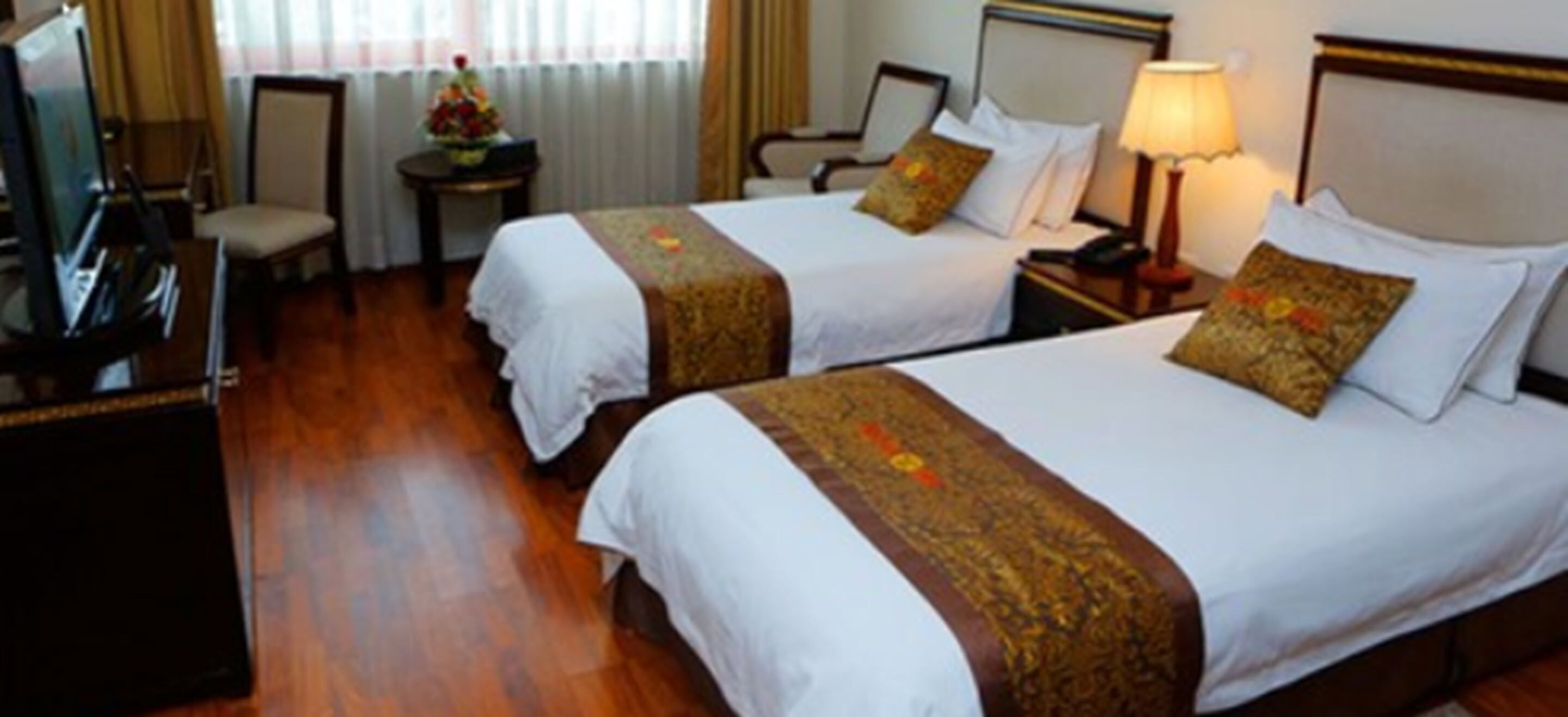 Een hotelkamer met twee bedden, een televisie, een bureau en een lamp.