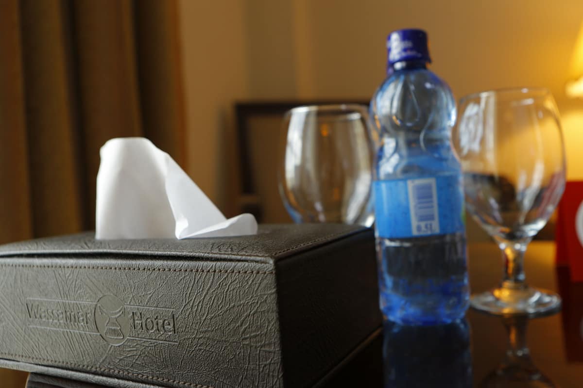 A hotel room with a tissue box, a water bottle, and two wine glasses on a table.