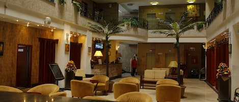 Un vestíbulo de hotel con mostrador de recepción, zona de estar y varios pisos con balcones.