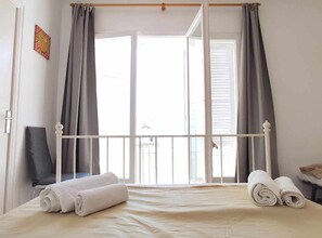 Ein Schlafzimmer mit Bett, Vorhängen, einem Sessel und einem Fenster.