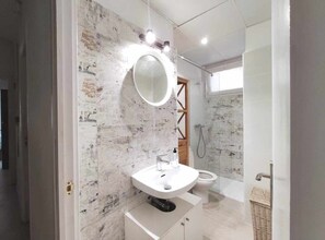 Ein modernes Badezimmer mit Marmorwand, einem runden Spiegel, einem weißen Waschbecken und einer Duschkabine.