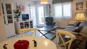 Una sala de estar con sofá, sillones, una mesa de centro de vidrio, televisor y un aparador con adornos.
