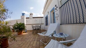 Un patio con dos sillones blancos, una mesita y plantas en macetas.