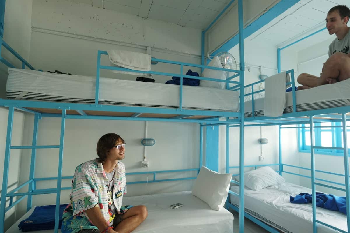 A dormitory room with bunk beds, a fan, and a window.