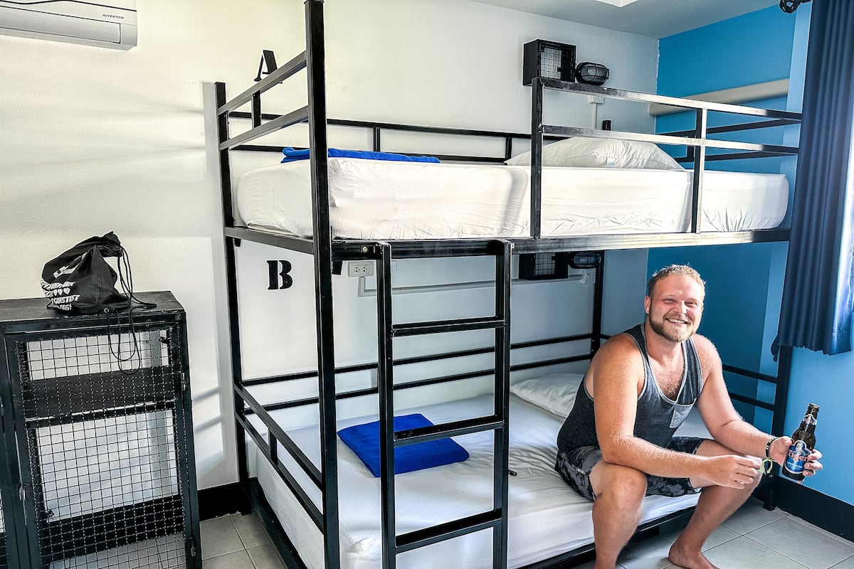 A bunk bed room with a black metal frame, a blue pillow on the lower bunk, and a black bag on a shelf.
