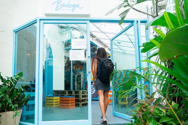 A glass-fronted entrance to Bodega Hostels with a sign indicating late check-in and early check-out policies. - Bodega Party City Center Bangkok - Hostel (Bangkok)