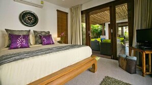 A bedroom with a large bed, a television on a wooden table, and a sliding glass door leading to an outdoor area with a sofa.
