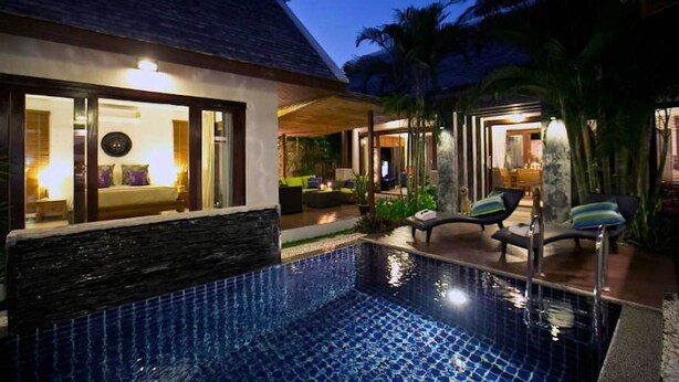 A modern hotel with a swimming pool, outdoor seating, and a well-lit interior.
