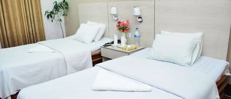A hotel room with two single beds, a nightstand with a lamp, a vase with flowers, and a bottle of water.