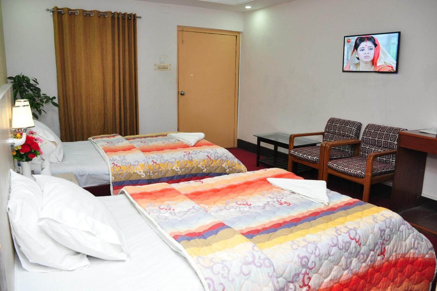 A hotel room with two beds, a desk, a chair, a TV, and a door.