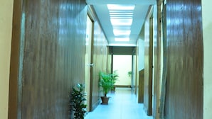Um corredor comprido e estreito com paredes de madeira e chão de azulejos, que leva a um quarto iluminado com uma luminária no teto.