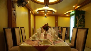 Uma sala de jantar com mesa posta para quatro, cadeiras, um ventilador e um vaso decorativo.