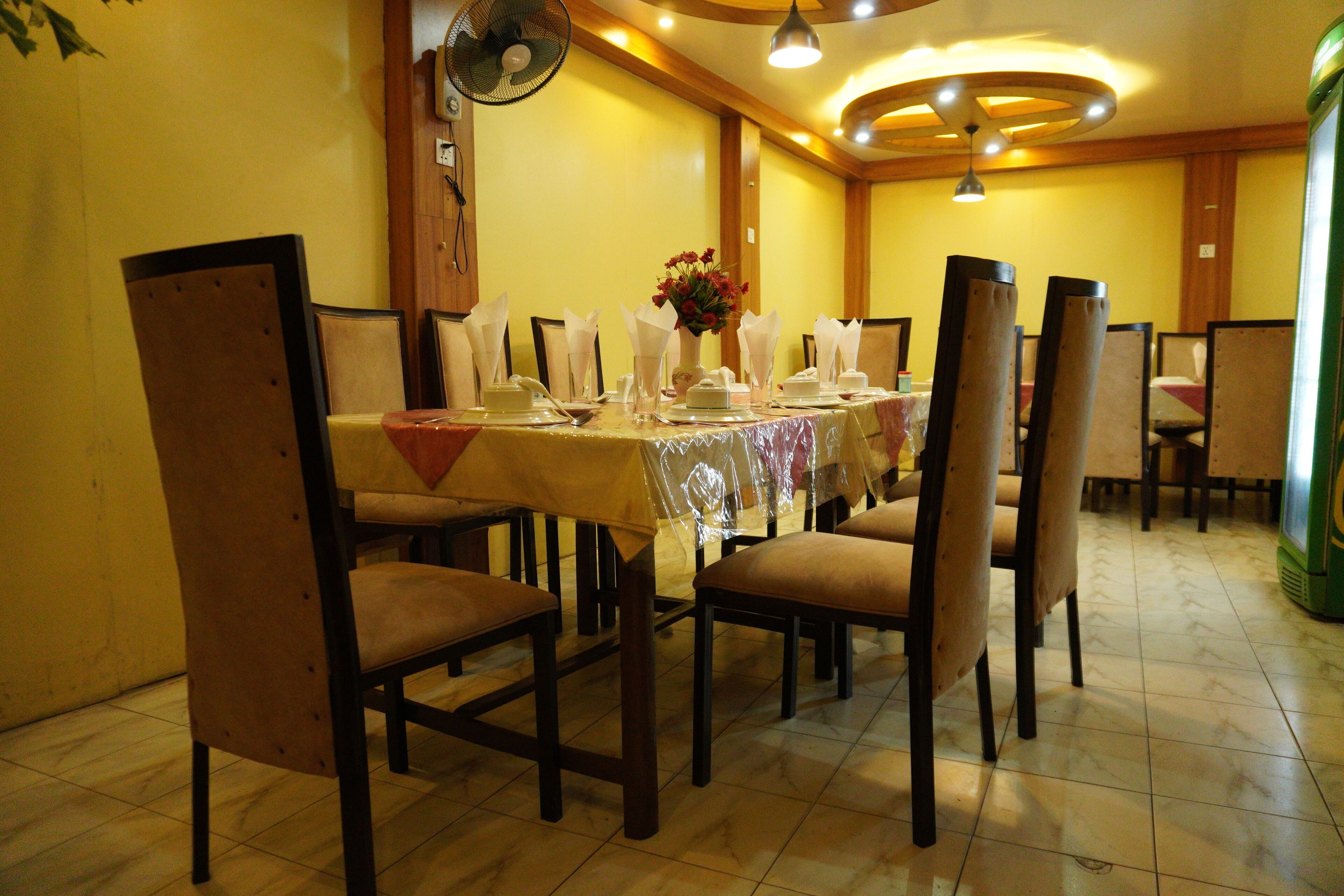 Un comedor con una mesa dispuesta para seis personas, rodeada de sillas, un ventilador y un jarrón decorativo.