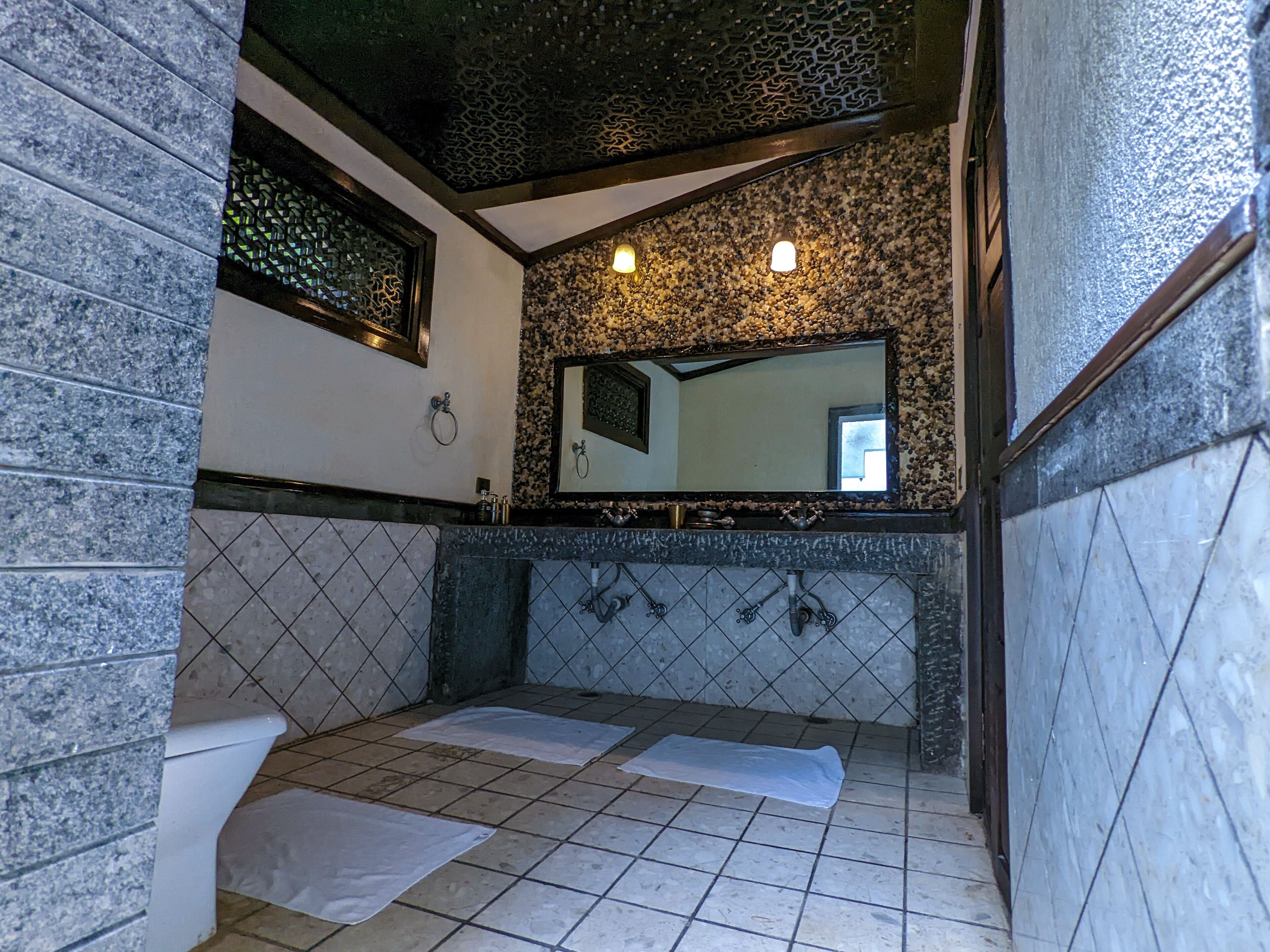 A bathroom with a tiled floor, a sink with a mirror above it, and a towel rack on the wall.