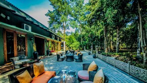 An outdoor seating area with sofas, tables, and chairs, surrounded by trees and a decorative fence. - Syna Tiger Resort - Bandhavgarh (Manpur)