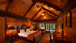 A wooden cabin bedroom with a bed, bedside tables, a desk, and a ceiling fan. - Syna Tiger Resort - Bandhavgarh (Manpur)