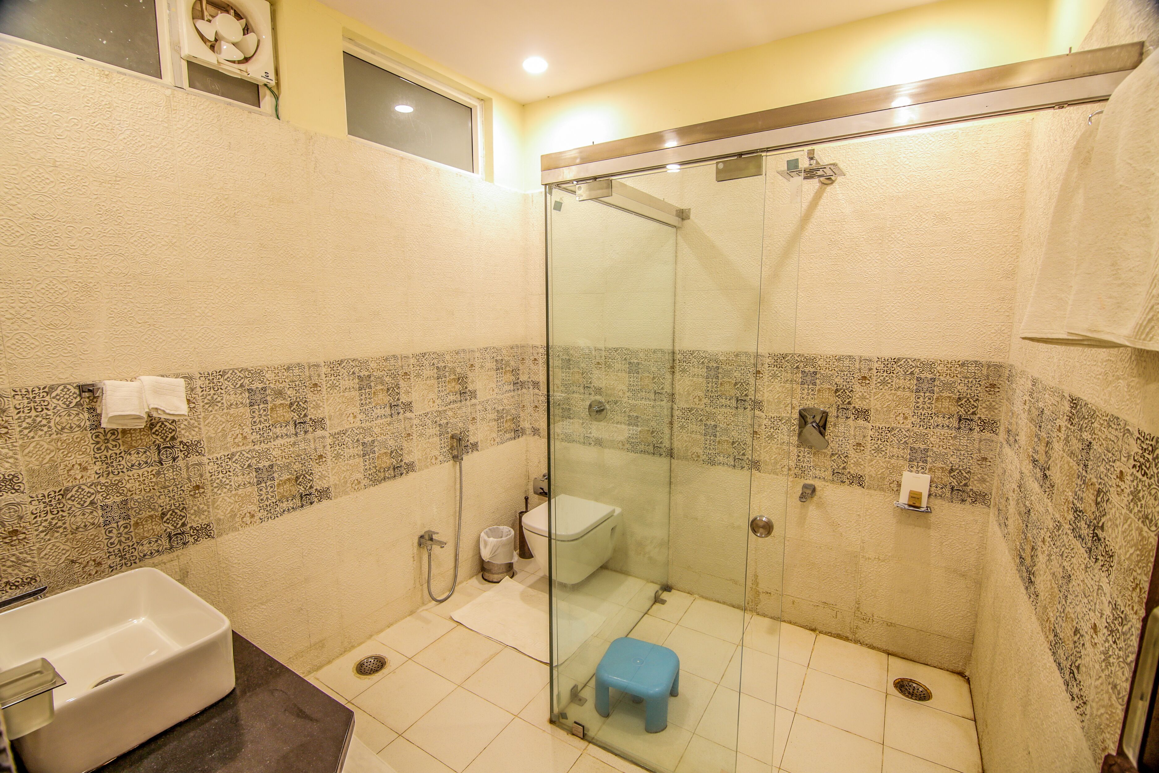 A bathroom with a glass-enclosed shower, a white toilet, and a small blue stool.