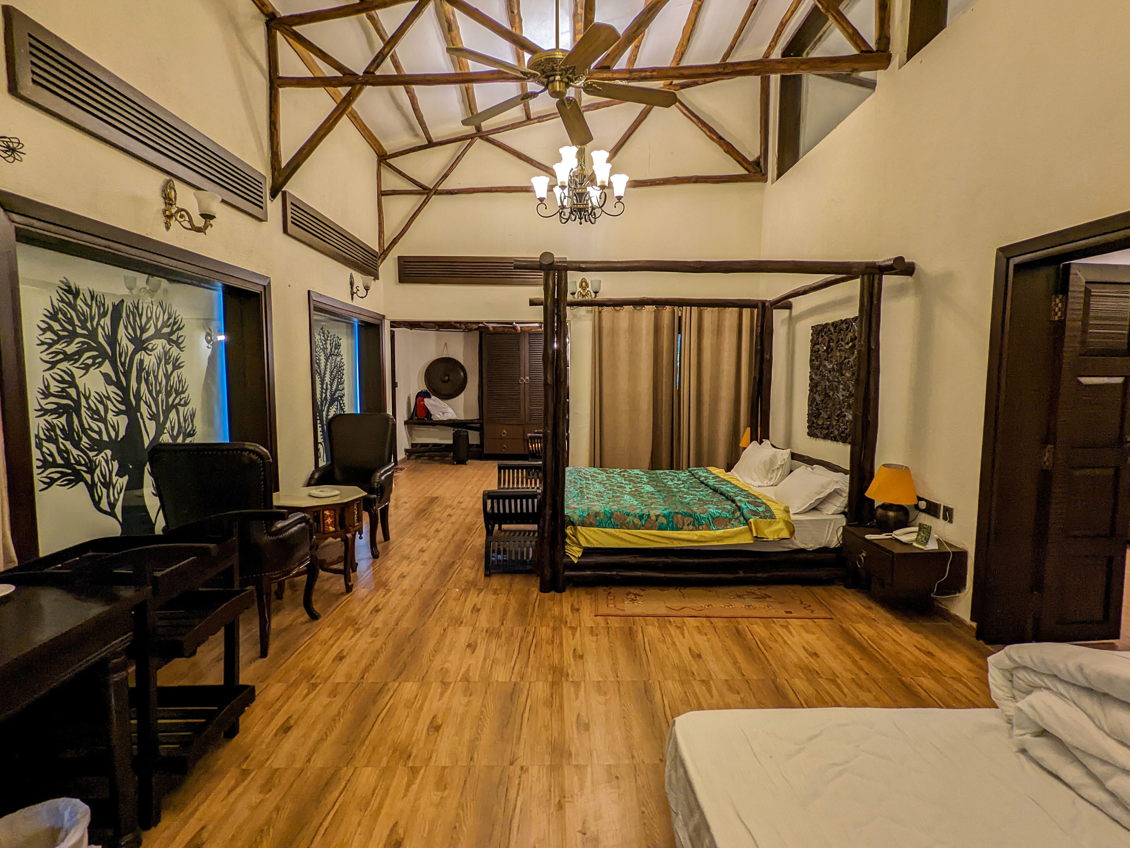 Quarto com cama de dossel, piso de madeira, lustre e uma grande janela com cortinas.