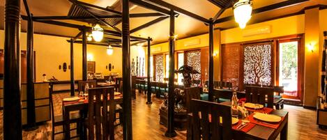 A restaurant with wooden flooring, dark wooden tables and chairs, and hanging light fixtures.